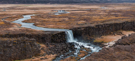 Aerial View of Majestic Waterfall Flowing into River in Icelands Barren Landscapeの写真素材