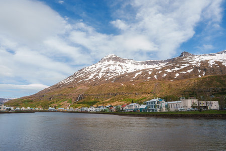 Charming Icelandic Town with Snow-Capped Mountain and Waterfall in Backgroundの写真素材