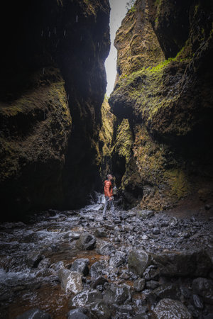 Person in Bright Orange Jacket Standing in Narrow Moss-Covered Canyon in Icelandの写真素材