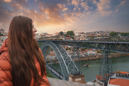 Woman in Orange Jacket Admiring Dom Luis I Bridge at Sunset in Porto