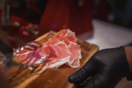 Close-Up of Thinly Sliced Prosciutto on Wooden Cutting Board in Luxury Settingの写真素材