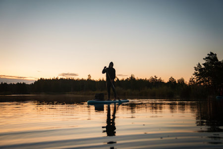 Person on Stand-Up Paddleboard at Sunrise on a Calm Lake with Tree Line