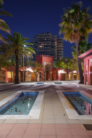 Nighttime Plaza with Water Features and Red Building in Benalmadenaの写真素材