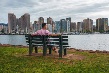 Man on Bench Overlooking Honolulu Skyline and Marina Waterfrontの写真素材