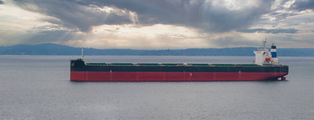 Large Cargo Ship with Red Hull on Calm Waters Under Dramatic Skyの写真素材