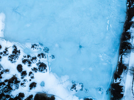 Frozen Lake with Snow Covered Terrain and Dark Circular Spot in Alpsの写真素材