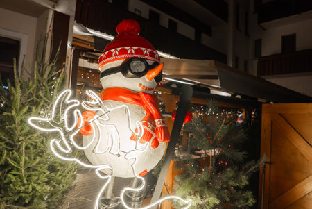 Festive Snowman with Neon Reindeer and Alpine Architecture in Winterの写真素材