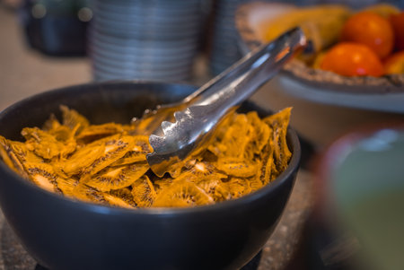 Close Up of Dried Kiwi Slices in Black Bowl with Metal Tongsの写真素材