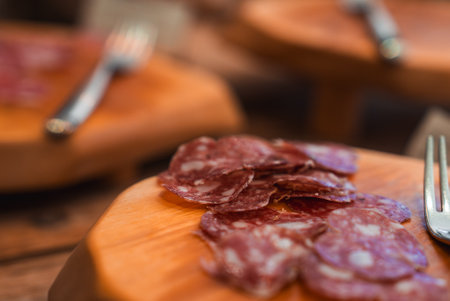 Thinly Sliced Salami on Wooden Board with Fork in Rustic Settingの写真素材