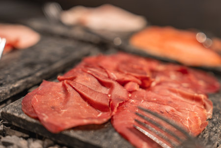 Close Up of Sliced Cured Meat on Dark Stone Platter with Forkの写真素材