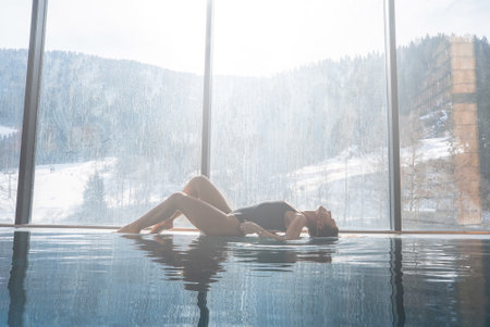 Woman Relaxing by Indoor Infinity Pool with Alpine Snowy Viewの写真素材