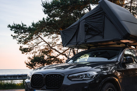 Modern SUV with Rooftop Tent in Forest Near Water at Sunsetの写真素材