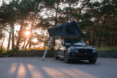Modern SUV with Foldable Rooftop Tent in a Forested Areaの写真素材