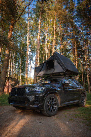 Modern Black SUV with Foldable Rooftop Tent in a Forested Areaの写真素材