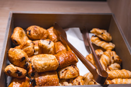 Wooden Box with Assorted Pastries and Bronze Tongs in Warm Lightingの写真素材