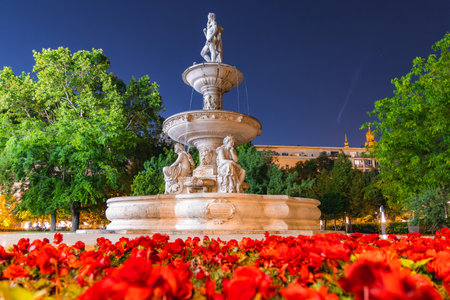Illuminated Fountain with Sculptures and Lit Spires at Nightの写真素材