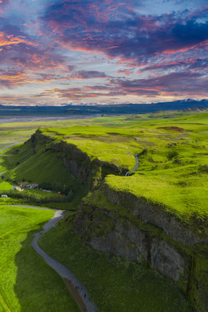 Aerial View of Icelandic Cliffs, Waterfall, and Vibrant Sunset Skyの写真素材
