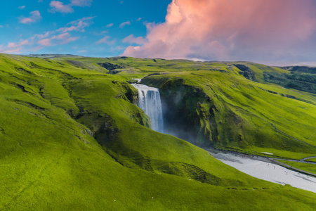 Aerial View of Skogafoss Waterfall and Surrounding Green Hills at Sunsetの写真素材