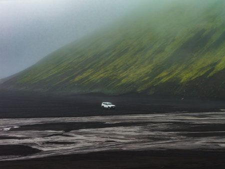 White Vehicle on Black Sand with Moss Covered Hill in Icelandの写真素材