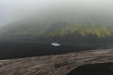 White SUV on Volcanic Plain with Mist Covered Hill in Iceland
