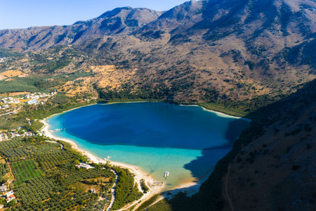 Aerial View of Lake Kournas with Boats and Mountain Backdropの写真素材