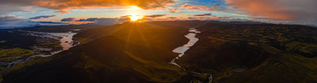 Aerial view of Iceland at sunset showing winding rivers, a serene lake, volcanic craters, snow capped glaciers, dark terrain, and dramatic clouds.の写真素材