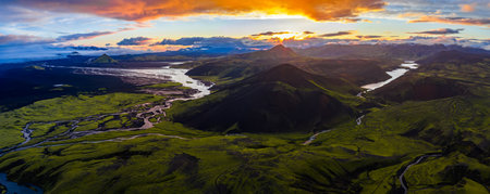 Aerial view of Iceland at sunset featuring a glacier, conical mountain, braided rivers, green valleys, volcanic hills, and a serene lake.の写真素材