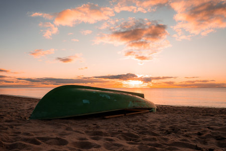 Green rowboat upside down on sandy beach at sunset, wide viewの写真素材
