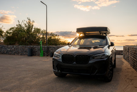 Luxury SUV with rooftop tent by stone seawall at sunset