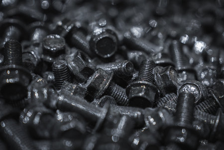 Close macro of black bolts and hex screws under harsh industrial lightの写真素材