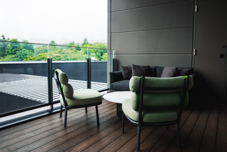 Hotel balcony lounge with mint chairs, gray sofa, and treetop viewsの写真素材