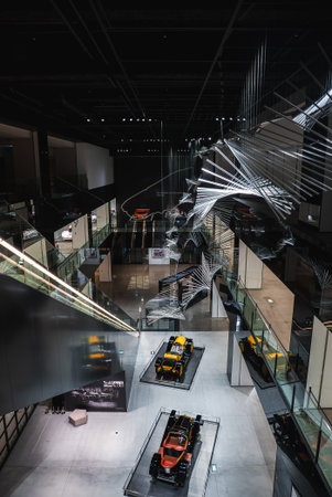 Multi level museum interior with race cars under metallic sculptures