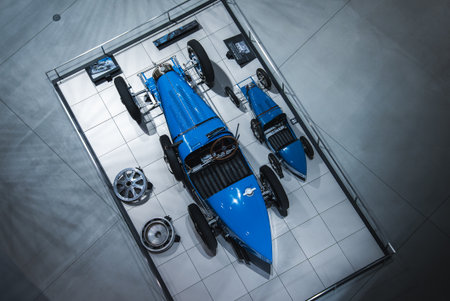 Overhead view of blue vintage race cars in a glass exhibit bay