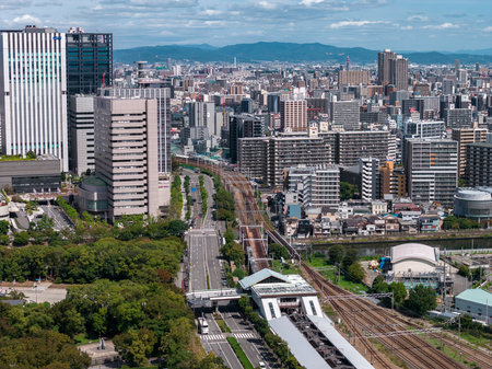 High angle daytime view of Osaka with railways, towers, and park beltの写真素材