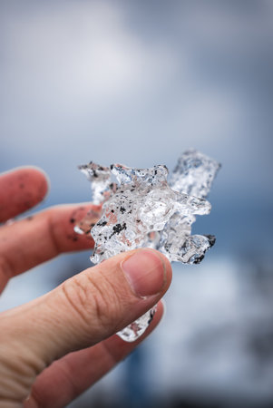 Hand holds ice shard with volcanic sand on Iceland coastの写真素材