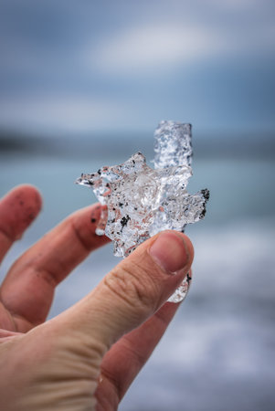 Hand holds glacier ice shard on Iceland coast near Diamond Beach