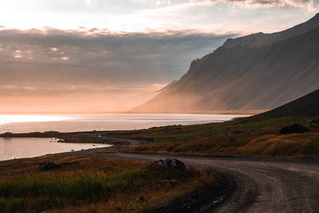 Gravel road along an Eastfjords fjord at peach sunset in Icelandの写真素材