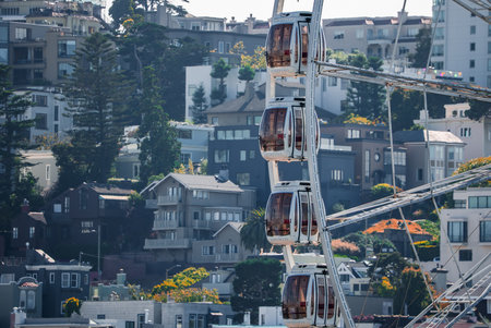 Ferris wheel gondolas rise before San Francisco hillside homesの写真素材