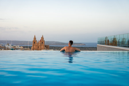 Rooftop infinity pool at dusk with Mellieha and sanctuary in viewの写真素材