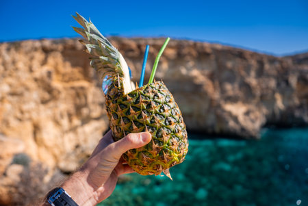 Hand holds pineapple drink at Blue Lagoon, Comino Island, Maltaの写真素材