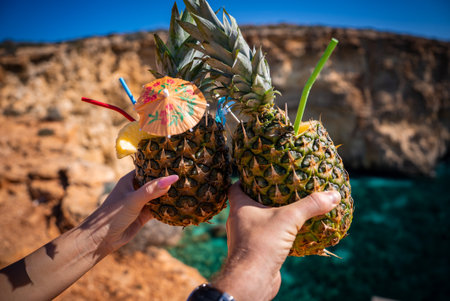 Pineapple drinks clink before limestone cliffs at Comino, Maltaの写真素材