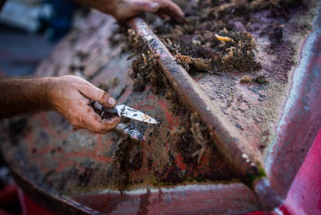 Fisherman scrapes marine growth from wooden boat hull in Marsaxlokk