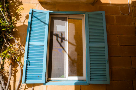 Sunlit window and turquoise shutters on limestone in Mdina, Maltaの写真素材