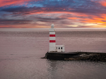 White and red banded lighthouse on rocky breakwater at sunset, Icelandの写真素材