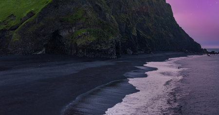 Reynisfjara black sand curves below cliffs at dusk in southern Icelandの写真素材