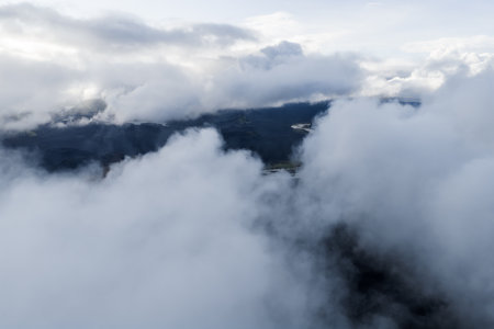 Aerial clouds drift over rugged highlands with a faint river belowの写真素材
