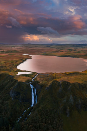 Aerial lake to waterfall over basalt cliffs in Iceland at sunsetの写真素材
