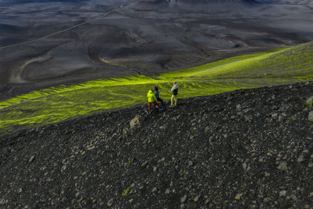 Hikers on volcanic slope view neon green moss in Iceland highlandsの写真素材