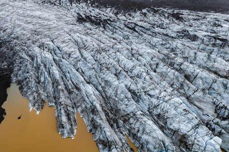 Aerial of Iceland glacier meeting rust meltwater lagoon under overcastの写真素材