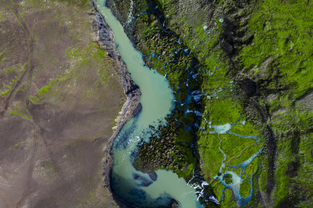 Aerial glacial river winding through Icelandic highland basalt and moss